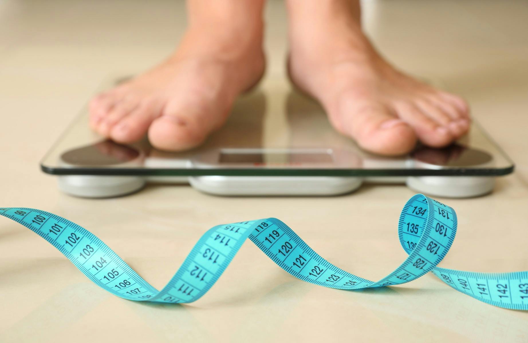 Feet on weighing scales with measuring tape in front of it